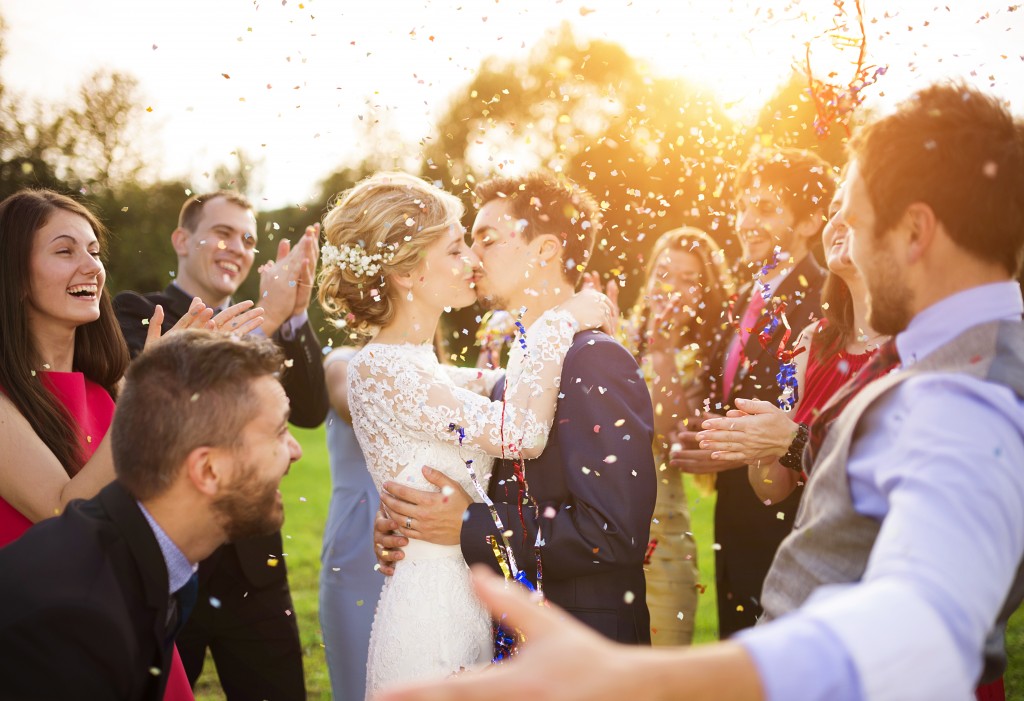 A picture of a groom kissing a bride while their friend happily throw rice into the air around them