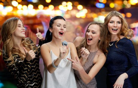 holidays, friends, bachelorette party, nightlife and people concept - three women in evening dresses with microphone singing karaoke over night club disco lights background
